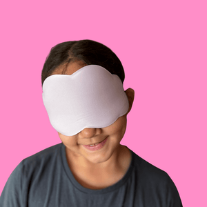 Little girl wearing a cloud shaped sleep mask against a pink background
