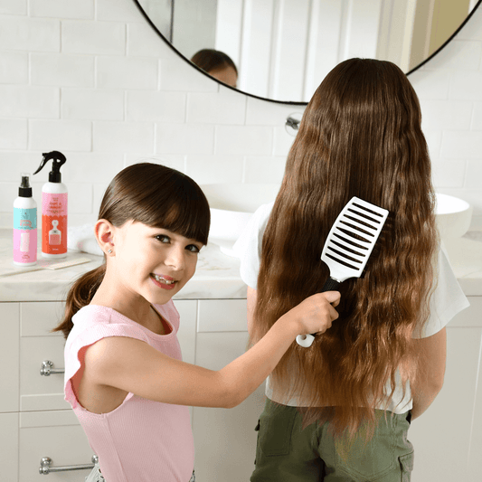 Two No Nasties detangling hairbrushes held by hands against a colourful abstract background