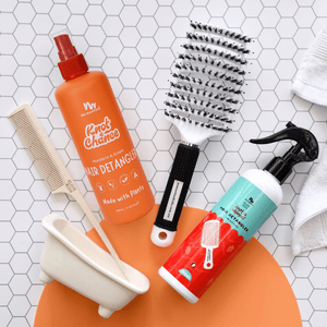 Hair care products including a bottle, brush, and comb on a tiled surface