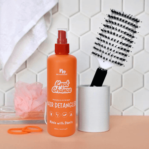 Orange hair detangler bottle with a brush and towel on a tiled bathroom counter