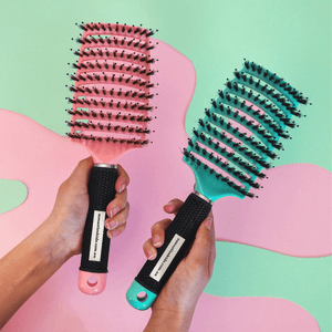 Two No Nasties detangling hairbrushes held by hands against a colourful abstract background