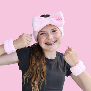 Girl wearing fluffy headband and arm cuffs for washing her face on pink background