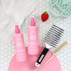 Two pink hair detangling sprays on a pink stand with a comb and brush on a tiled surface.