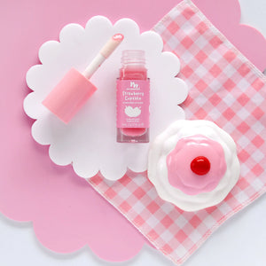 Pink strawberry lip gloss placed on a pink and white checkered cloth.