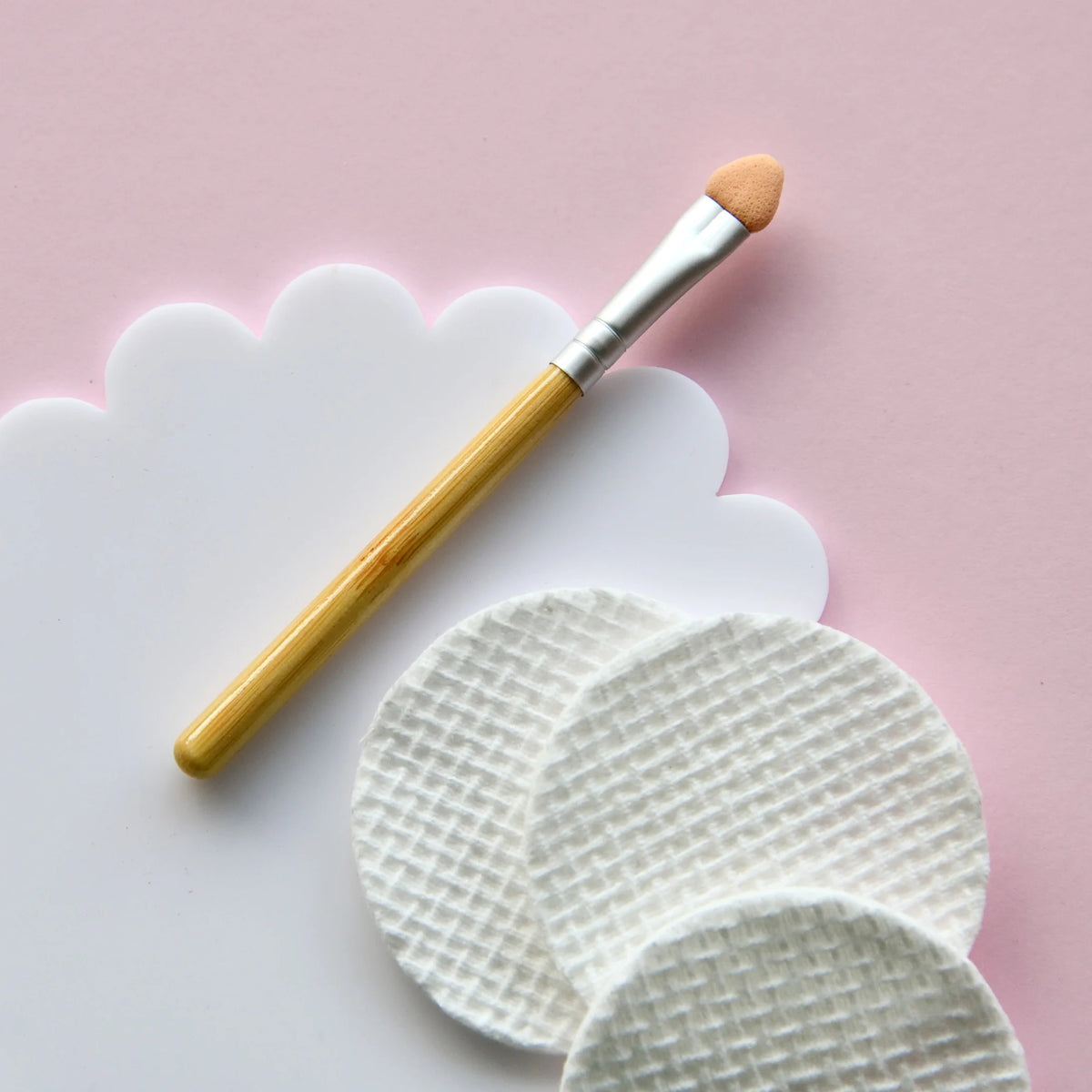 Makeup brush with wooden handle and white bristles on a pink background