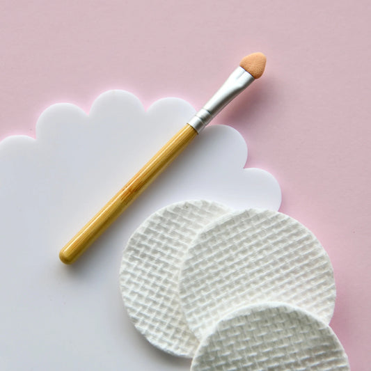 Makeup brush with wooden handle and white bristles on a pink background