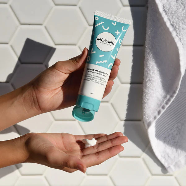 Hand holding a Mebeme skincare tube with a white towel in the background