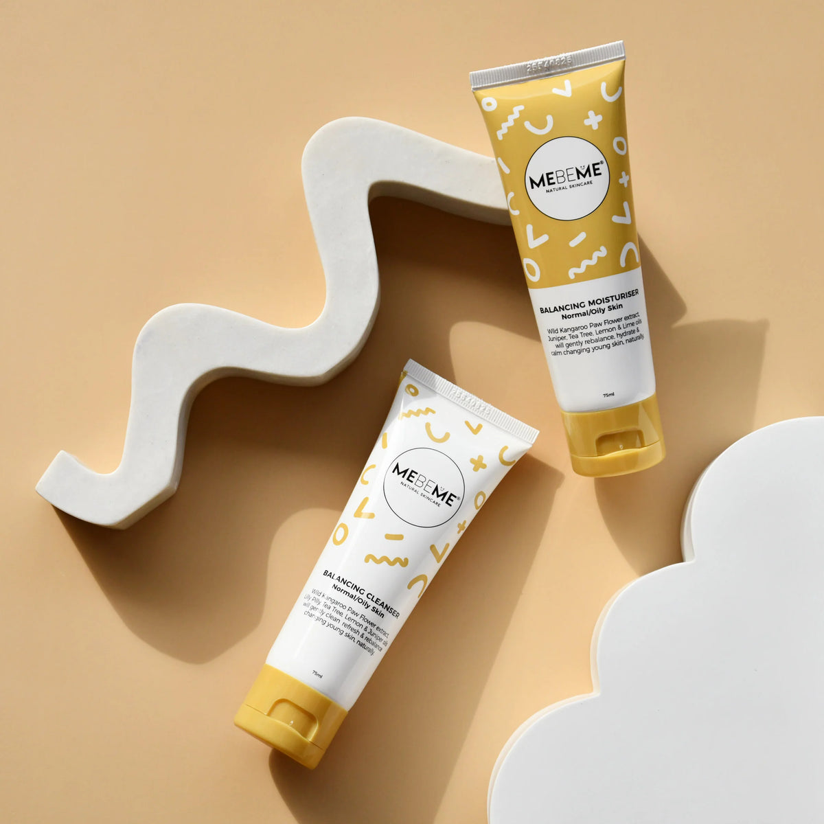 Two ME&M skincare products on a beige background with abstract shapes.