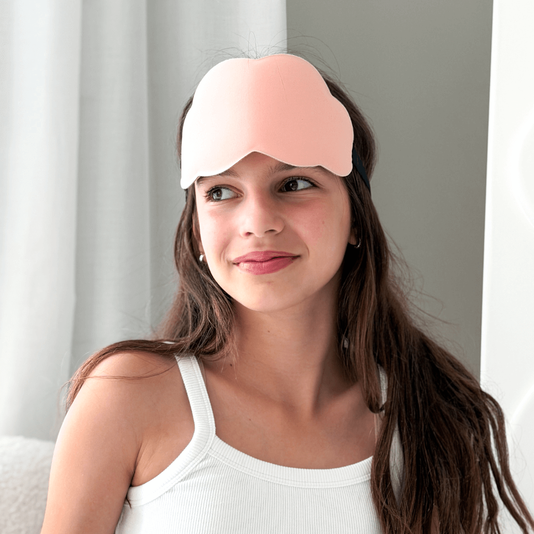 Girl wearing a pink sleep mask with a neutral background