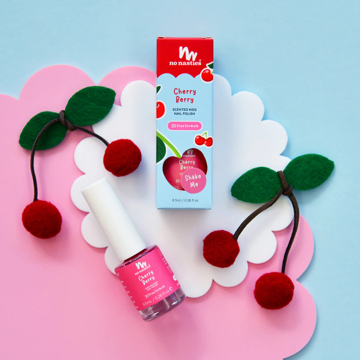 bright pink kids nail polish in packaging and outside on blue and pink background with felt cherries

