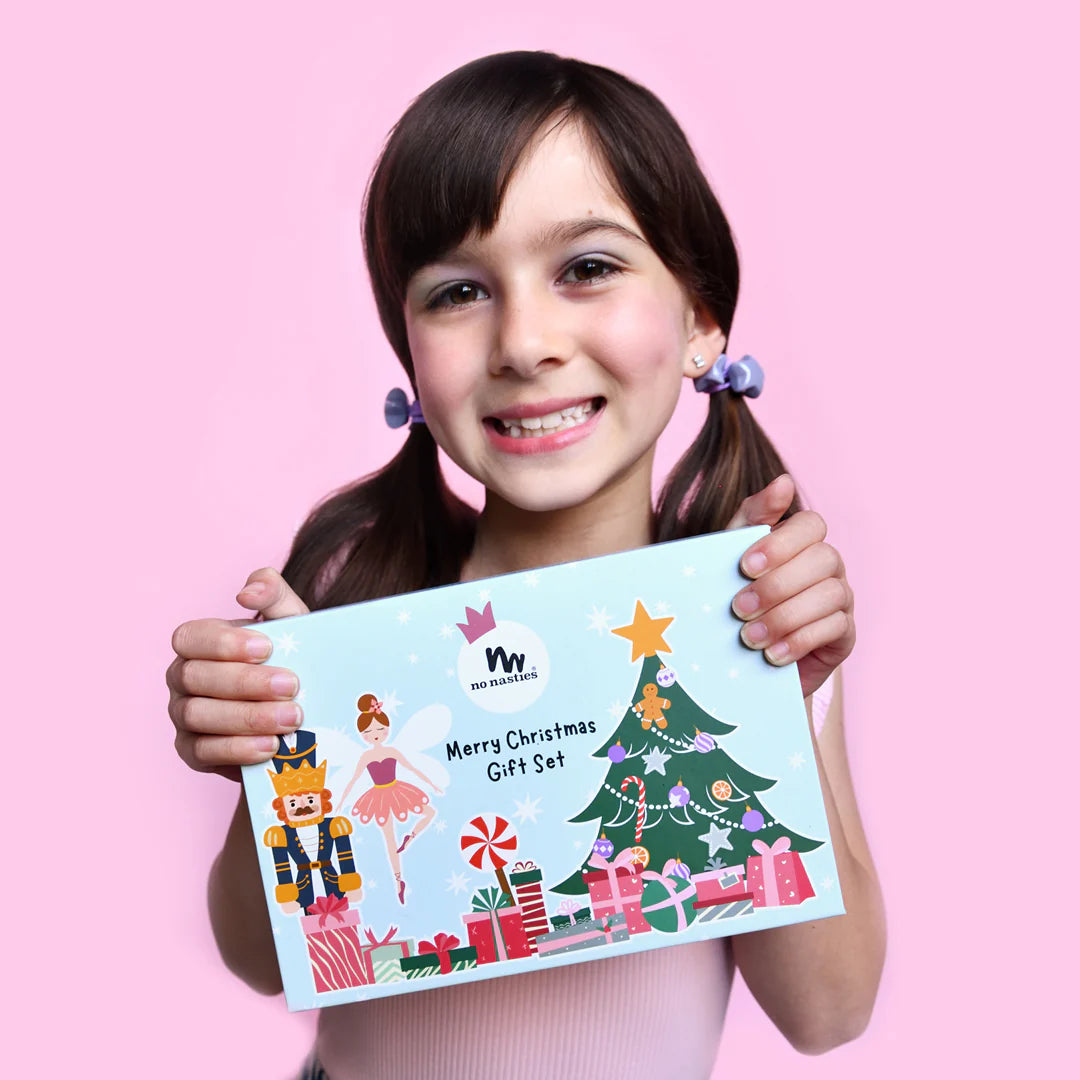 Young girl holding a Christmas-themed gift set packaging against a pink background