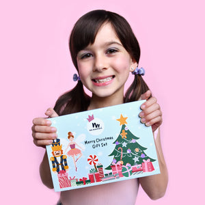 Young girl holding a Christmas-themed gift set packaging against a pink background