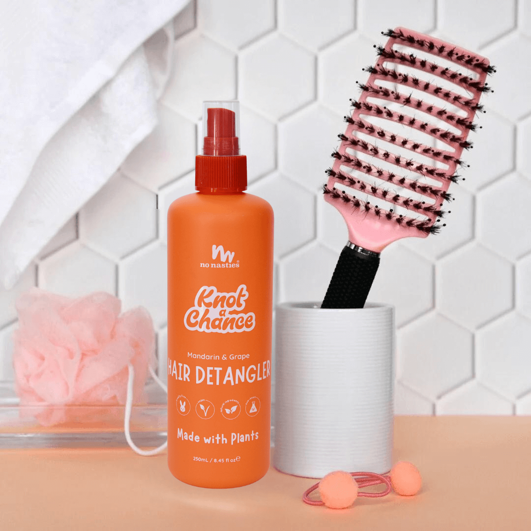 Orange bottle of hair detangler with a brush and accessories on a tiled background