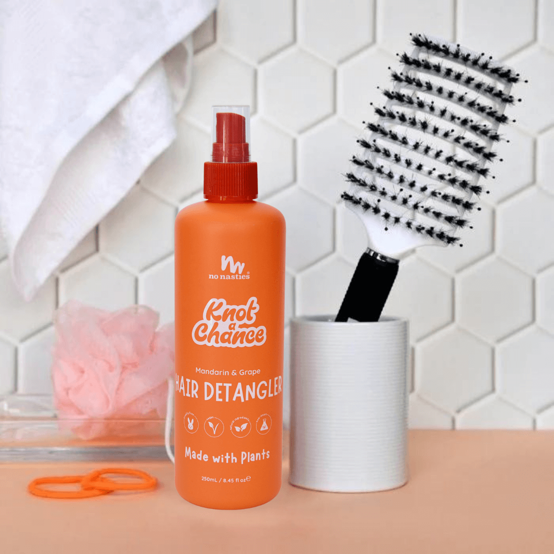 Orange hair detangler bottle with a brush and towel on a tiled bathroom counter