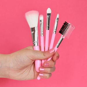 Set of makeup brushes with pink handles held against a pink background