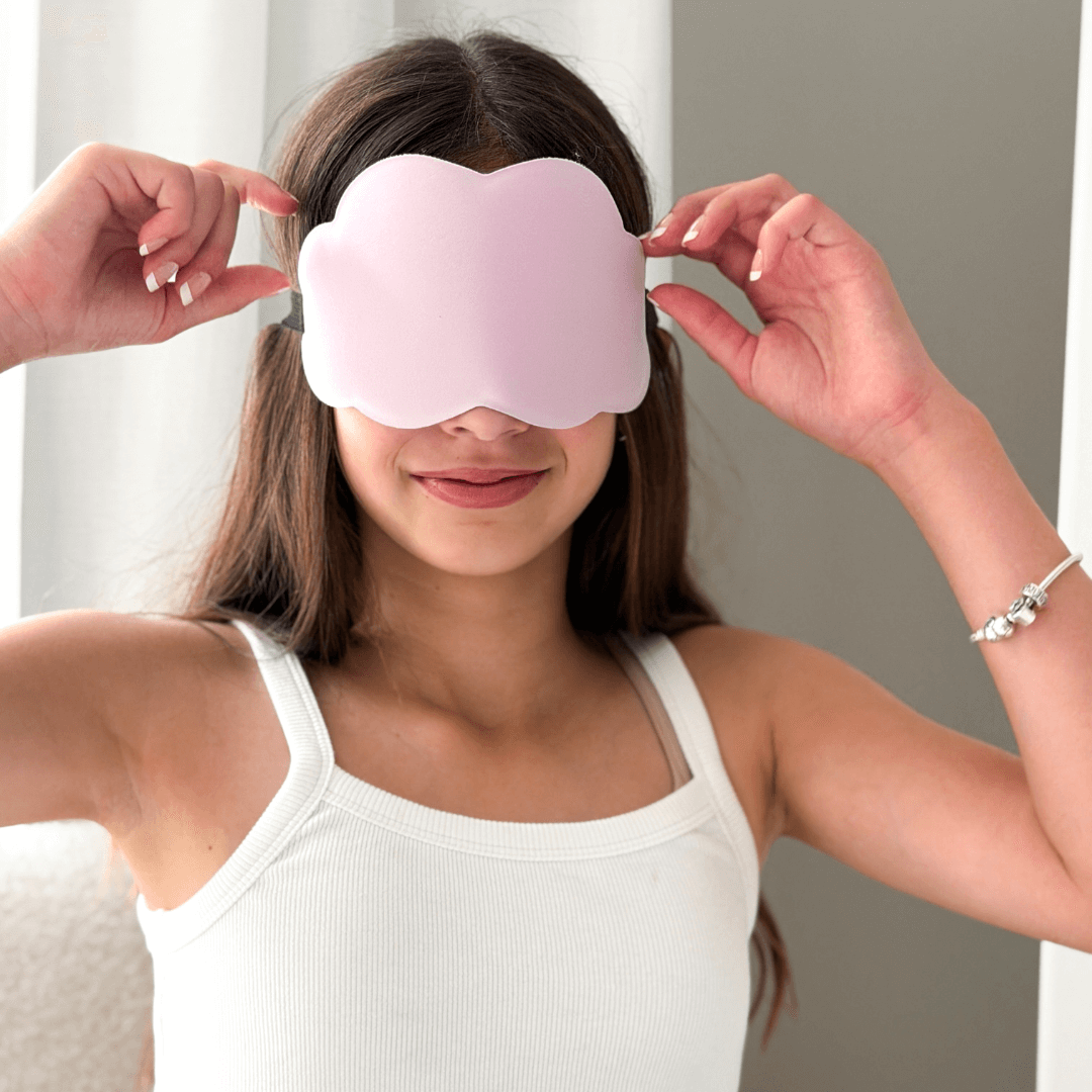 Girl wearing a lilac cloud shaped sleep mask with a neutral background