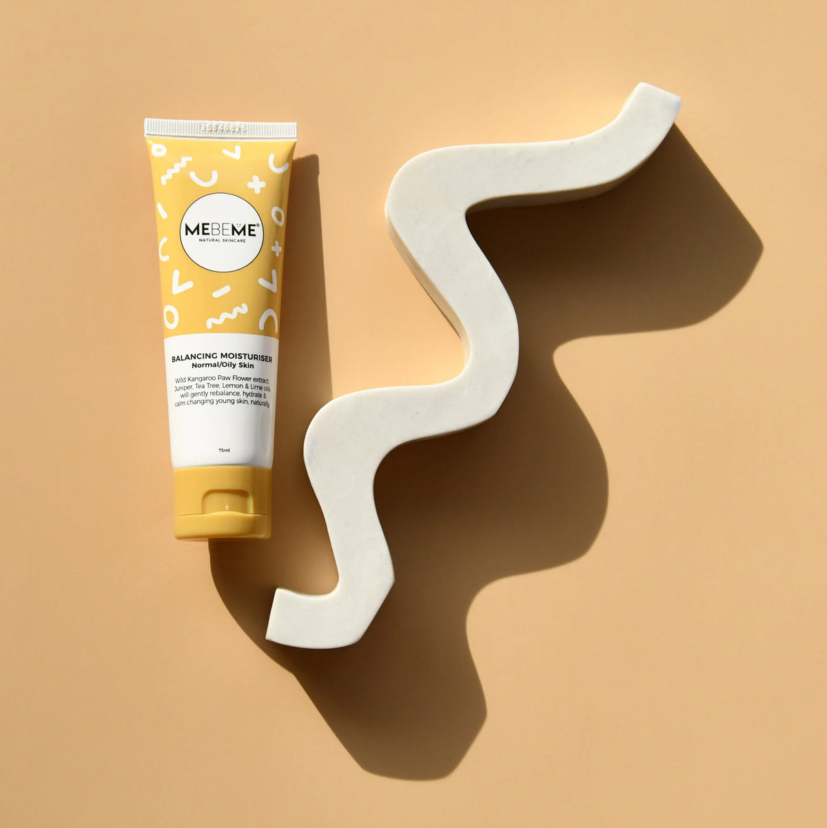 Tube of ME ME ME skincare product on a beige background with a wavy white object.