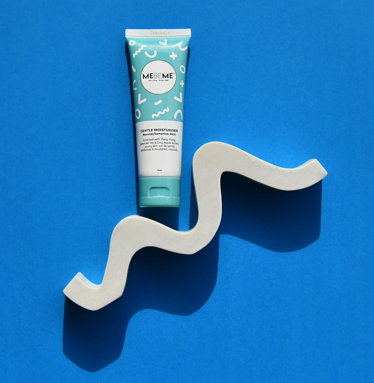 Tube of MEBEME hair product on a wavy grey stand against a blue background