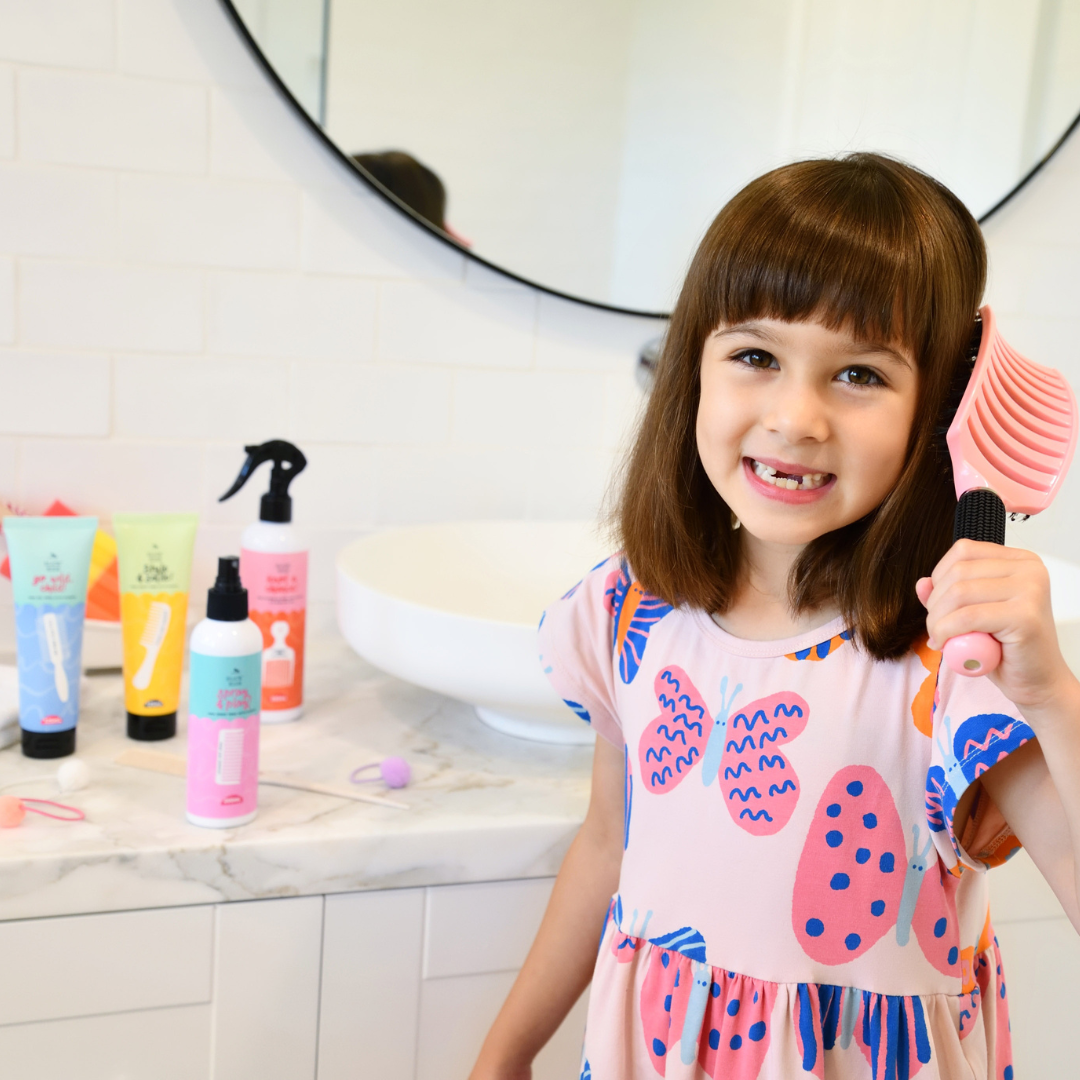 little girl brushing her hair with natural hair and body products on bathroom counter