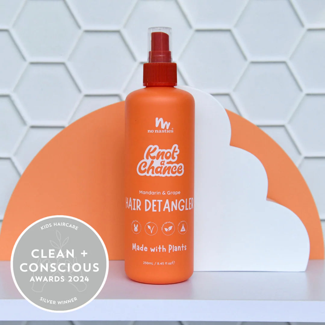 Orange hair detangler bottle with spray nozzle on a white surface against a geometric patterned wall.