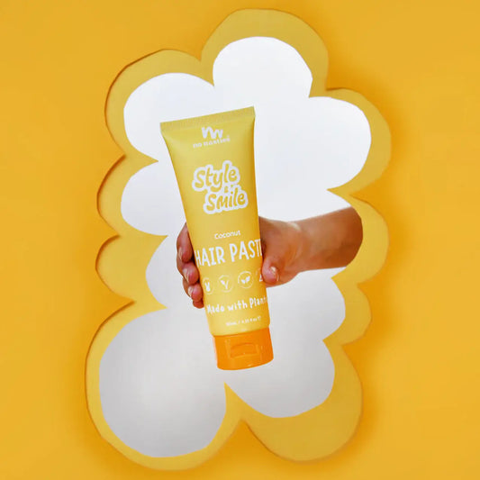 Hand holding a tube of No Nasties Style and Smile hair paste against a yellow background
