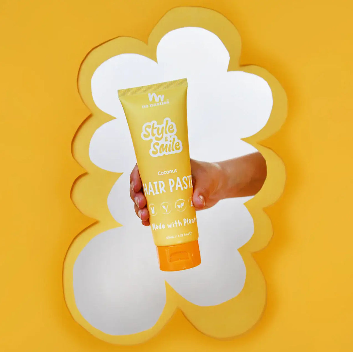Hand holding a tube of No Nasties Style and Smile hair paste against a yellow background