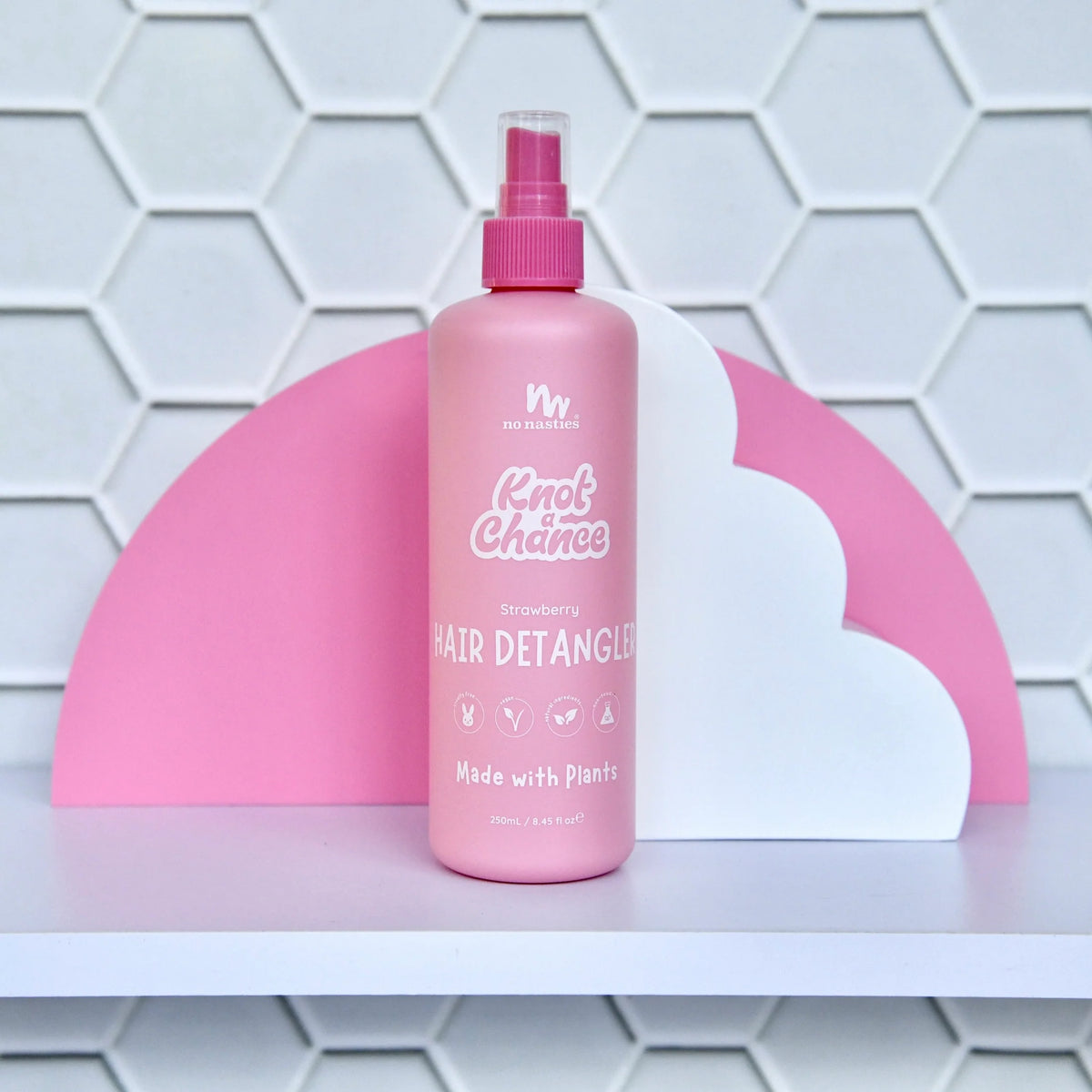 Pink hair detangler bottle with a spray nozzle on a white shelf against a tiled wall.