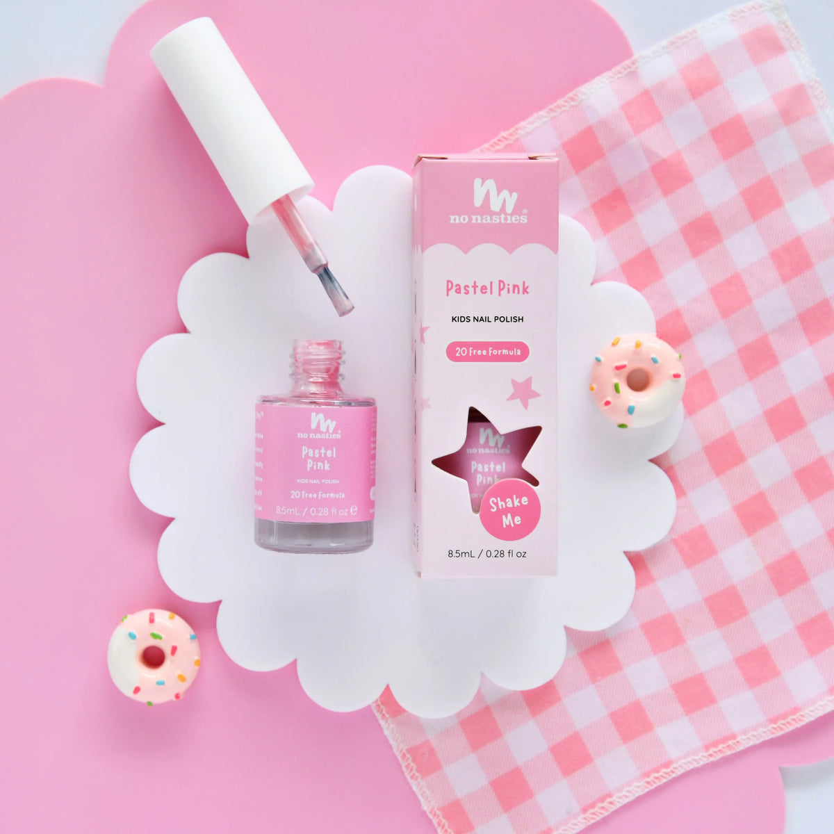 Pastel pink nail polish set with packaging and donut decorations on a pink background