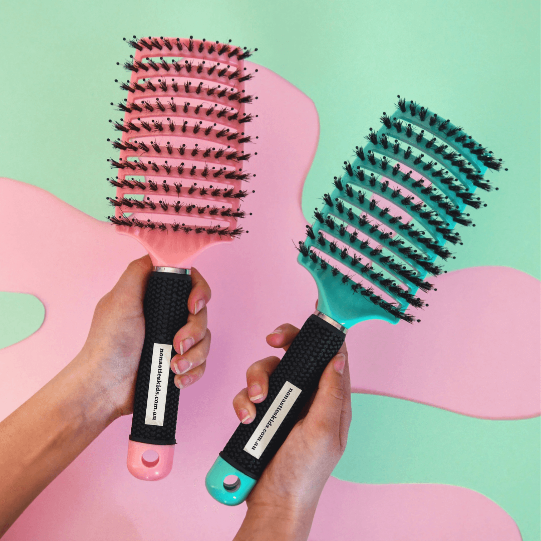 Two No Nasties detangling hairbrushes held by hands against a colourful abstract background