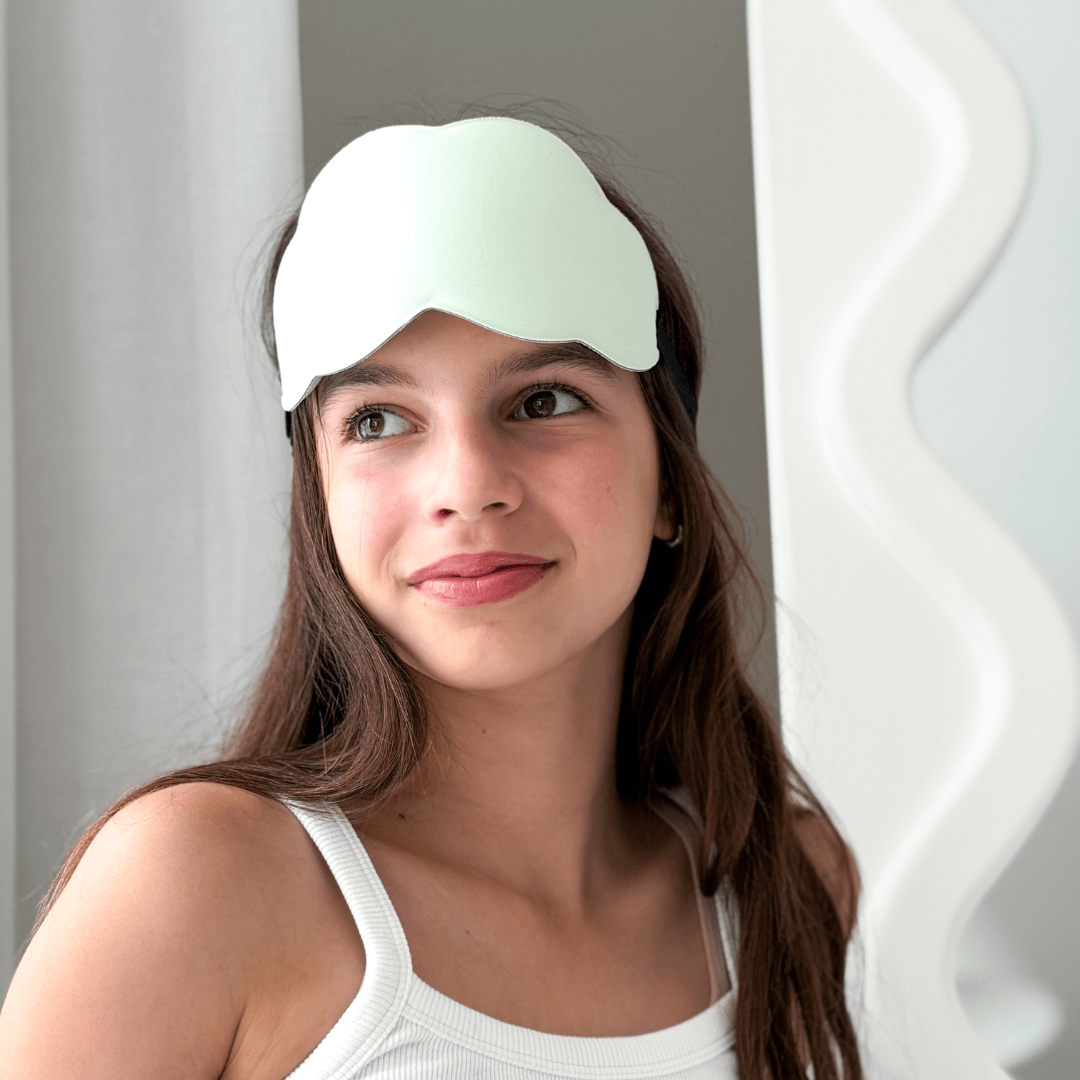 Tween wearing a light green sleep mask against a neutral background