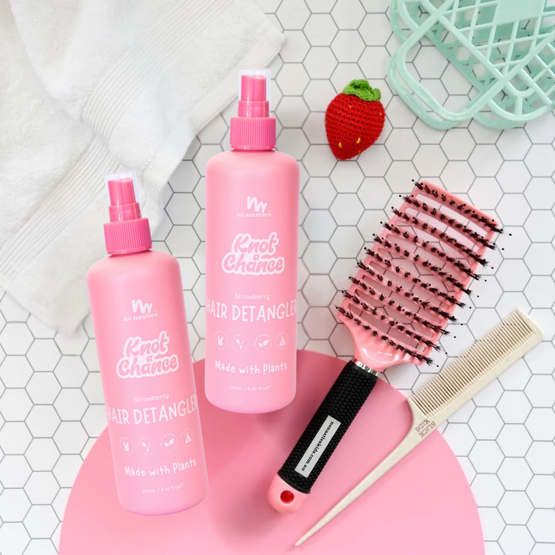 Pink hair detangler bottles with a brush and comb on a hexagonal tiled surface.
