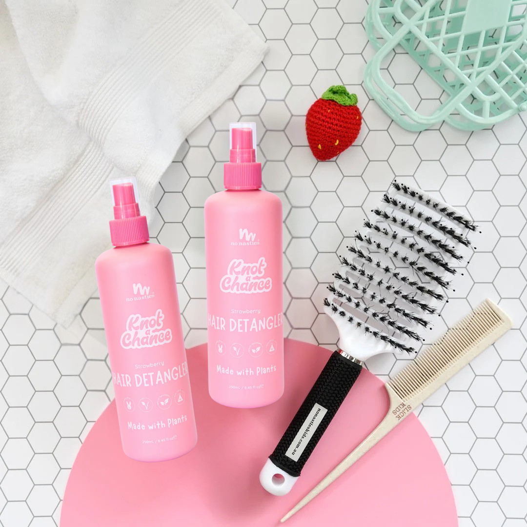 Two pink hair detangling sprays on a pink stand with a comb and brush on a tiled surface.