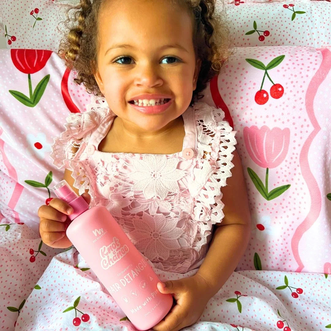 Child holding detangler spray with a floral patterned background