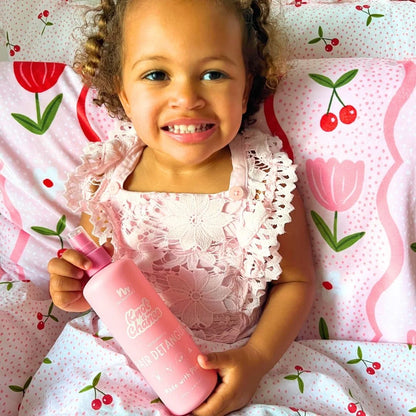 Child holding detangler spray with a floral patterned background