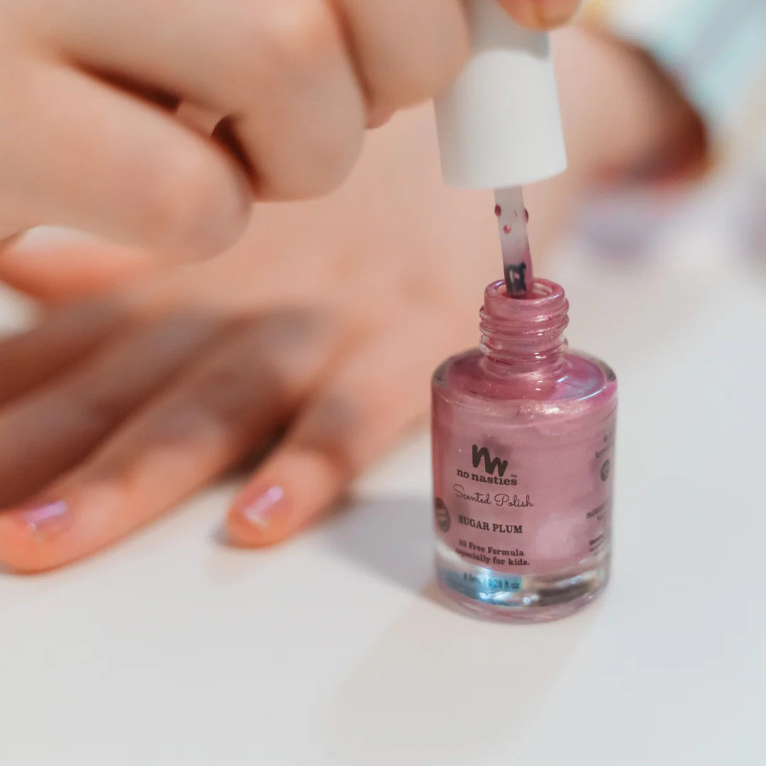 Person applying pink nail polish from a No Nasties Kids bottle on a white surface.