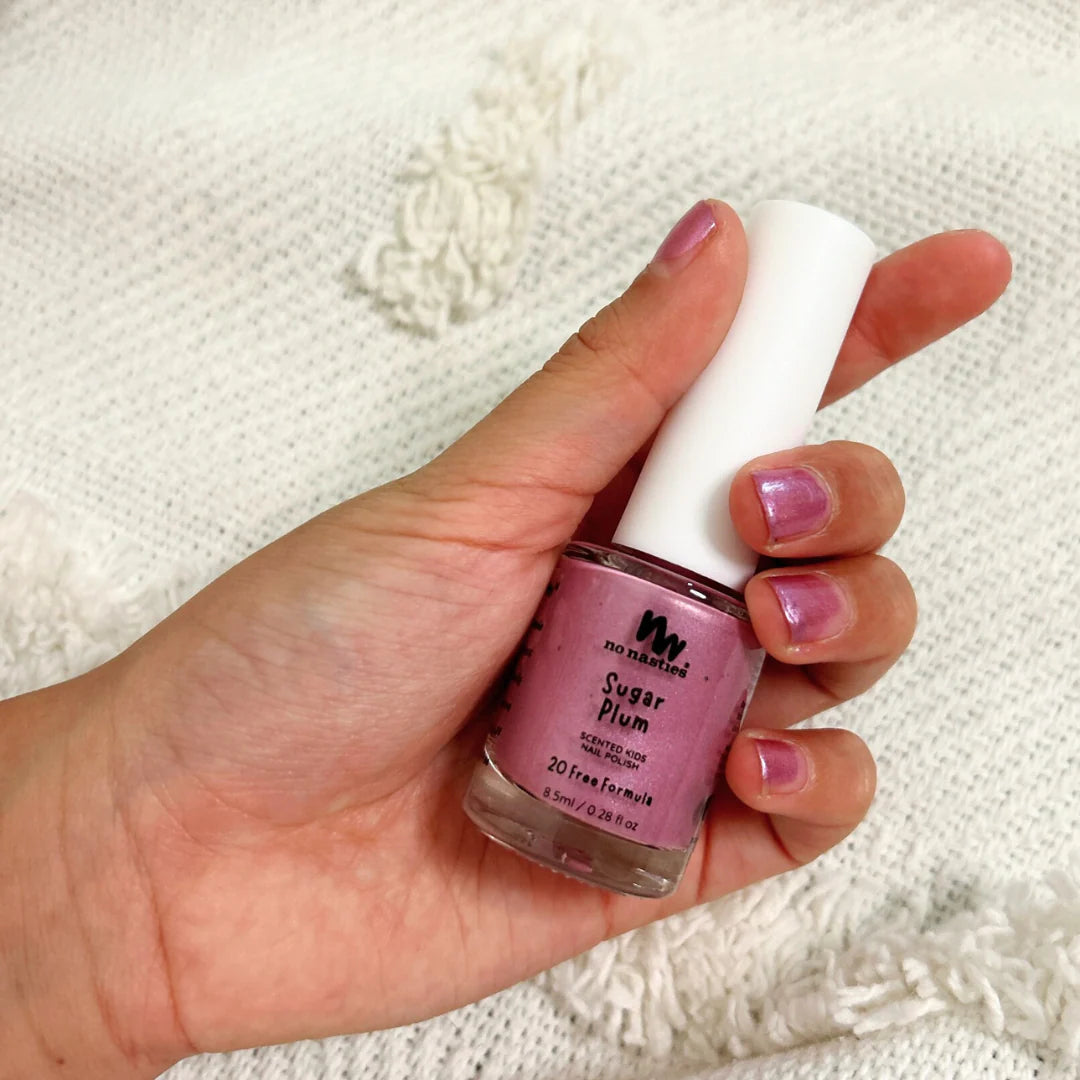 Hand holding a bottle of &#39;Sugar Plum&#39; nail polish with matching nails against a textured white background