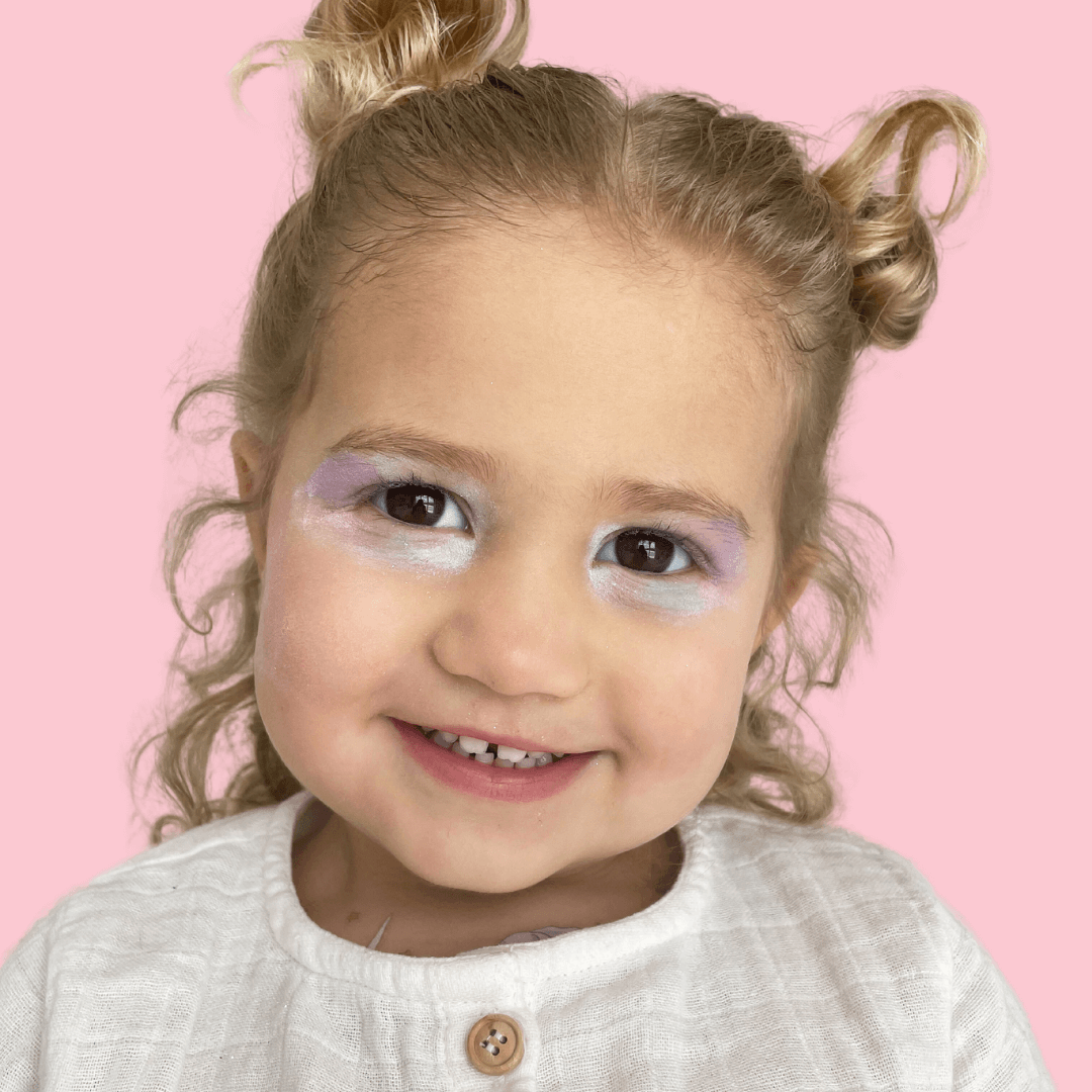 Pink makeup set for kids eyeshadow nail stickers and makeup brush laid out on pink background